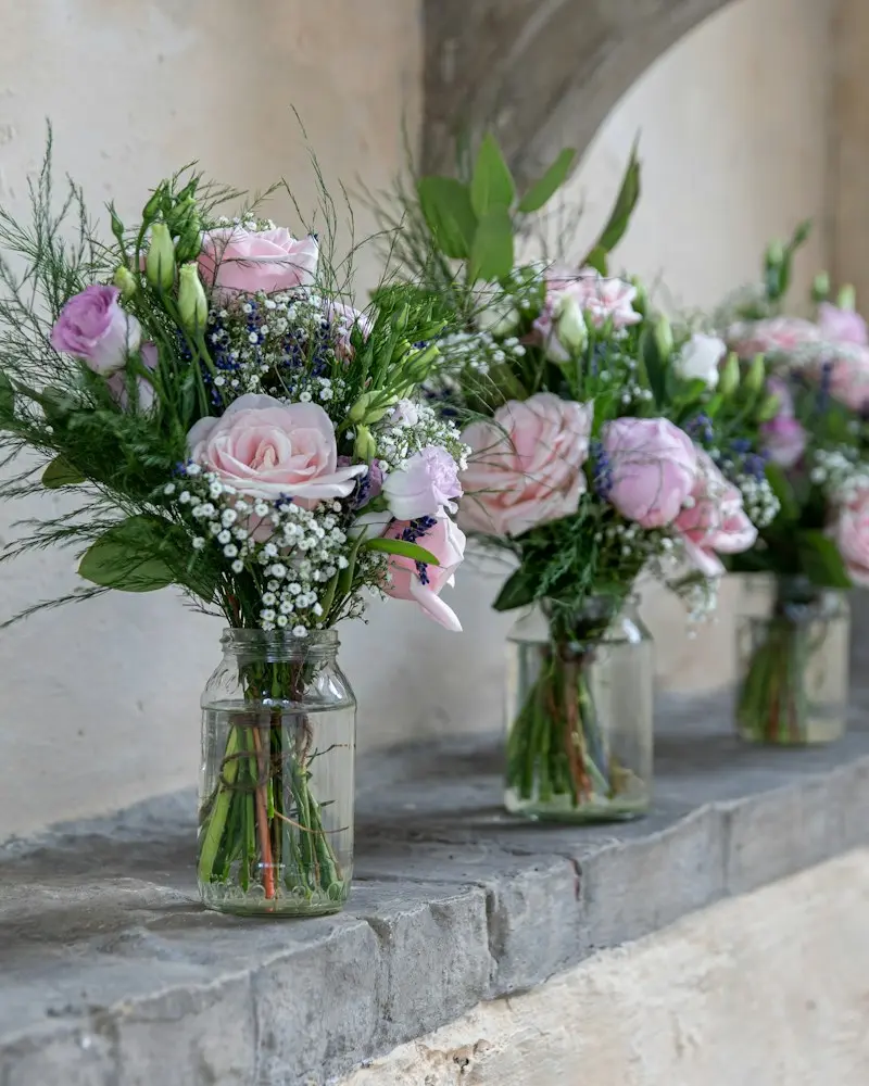 Glass jars of pink roses and white flowers on a stone window ledge