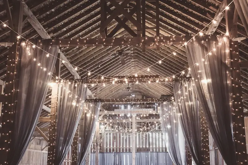A wooden hall with hundreds of string lights and sheer white drapes