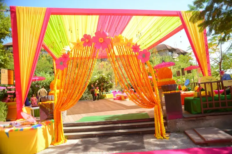 An outdoor entrance draped in yellow, orange and pink fabric with floral hoops