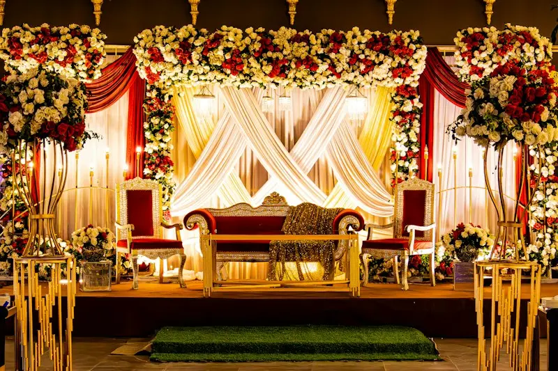 A reception stage with red and white flowers, draped fabric and a gold sofa